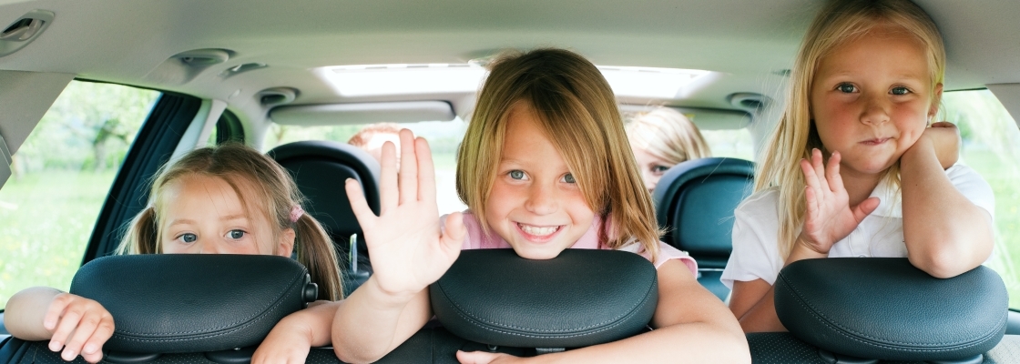 Three children smiling from the backseat of the car